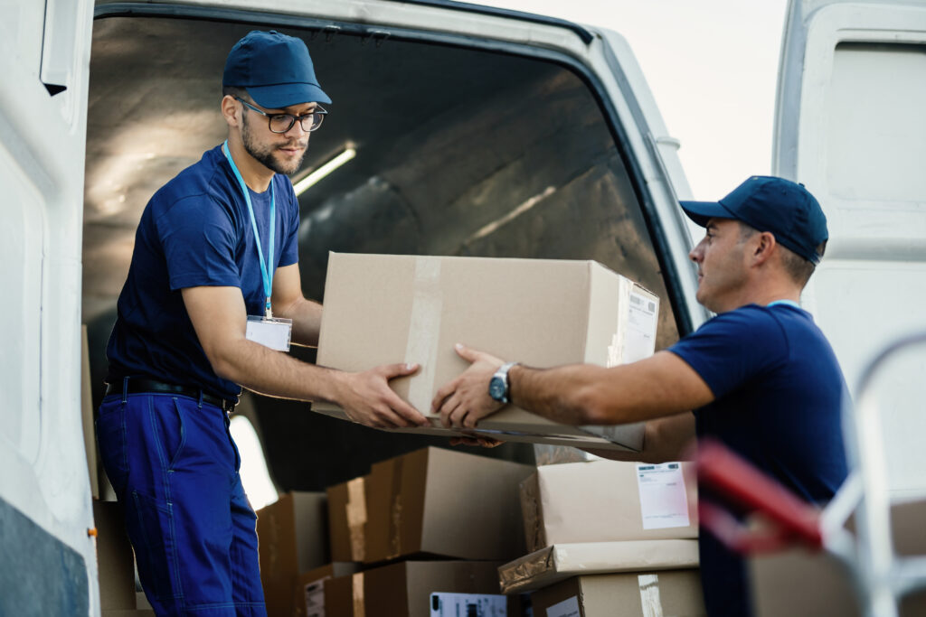 young couriers cooperating while unloading packages from deliver young couriers cooperating while unloading packages from deliver